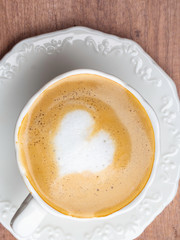 Close up white coffee cup with heart shape latte art on wood table at cafe.