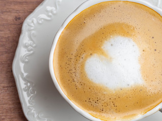 Close up white coffee cup with heart shape latte art on wood table at cafe.