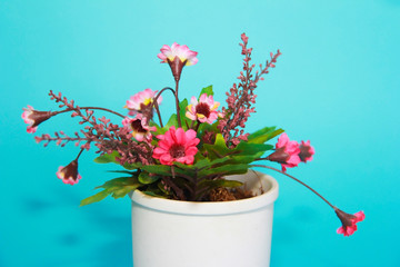 artificial pink flowers with green leaves in a white пот