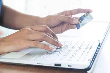 Woman hand holding plastic credit card and using laptop computer. Online shopping, paying, buying, e-payment and technology concept.
