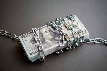 chained money, a bundle of dollars tied up with a chain, the concept of debt. dark background, closeup
