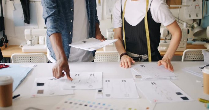 Clothes designers working with sketches putting papers on table pointing at creative designs planning new garments. Fashion and professionals concept.