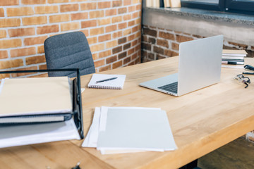 wooden desk with laptop and documents in loft office