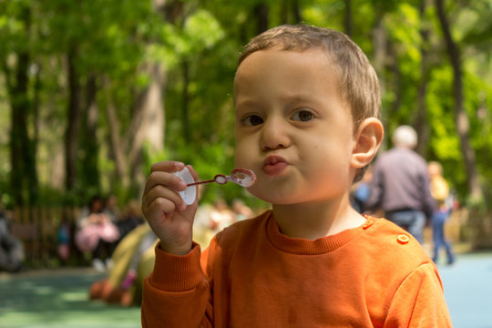 Portrait of sweet little boy blowing soap bubbles at a playground.