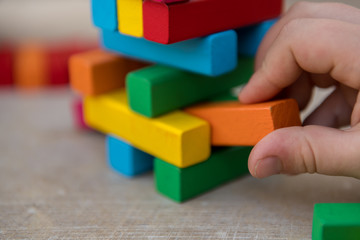 A child removes an orange wooden block from a tower with stacked wooden blocks.