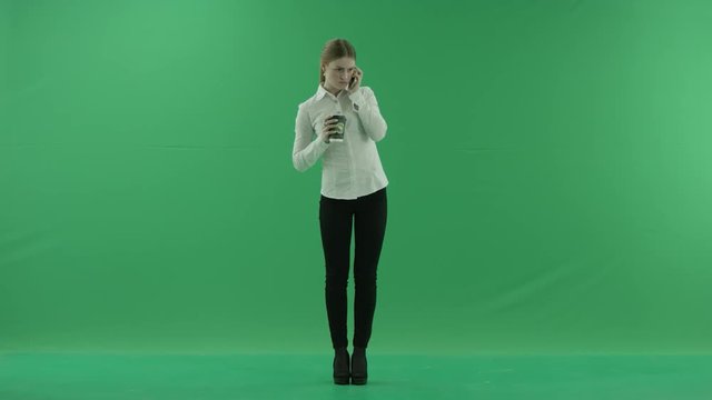 business woman is talking on her mobile cell phone with a cup of coffee or tea. She wears formal dress: white shirt and blak trousers. Businesswoman think, got idea and smile over green screen