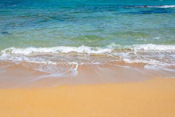 Fototapeta na wymiar Waves on a beach with orange sand and blue water