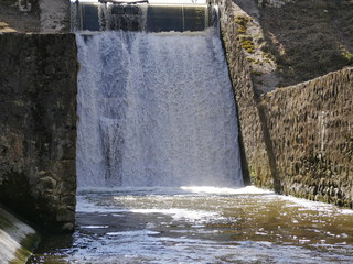 a powerful stream of water flows through the stone dam. sunny day. waterfall.