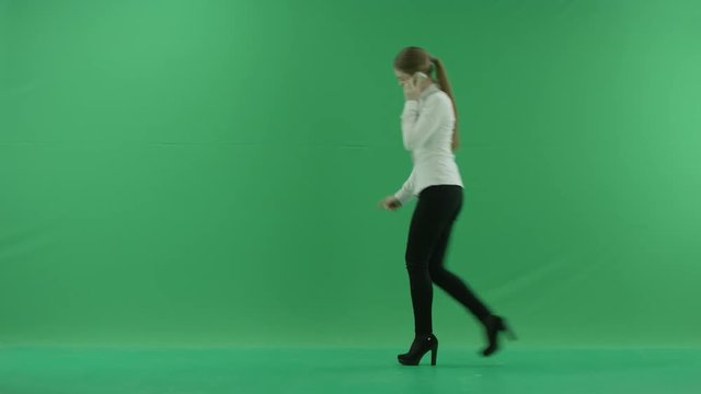 business woman is talking on her mobile cell phone and walking. She wears formal dress: white shirt and blak trousers. Businesswoman is over green screen