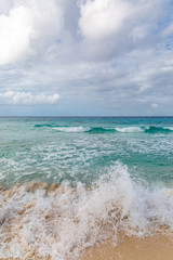 Fototapeta na wymiar Waves crashing onto a sandy beach, on the Caribbean Island of Barbados