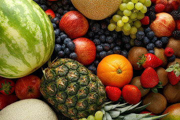 Variety of fresh fruits and berries on dark background: cantaloupe, melon, watermelon, blueberry, oranges, apple, strawberry, pineapple, mango, grapes and kiwi.