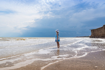 Beautiful seascape. Girl in dress and white hat on the beach over blue sky background