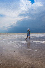 Beautiful seascape. Girl in dress and white hat on the beach over blue sky background