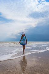Beautiful seascape. Girl in dress and white hat on the beach over blue sky background