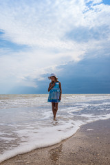 Beautiful seascape. Girl in dress and white hat on the beach over blue sky background