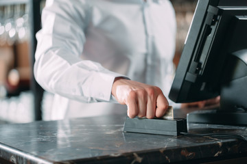 small business, people and service concept - happy man or waiter in apron at counter with cashbox working at bar or coffee shop.