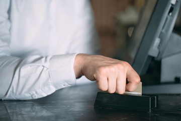 small business, people and service concept - happy man or waiter in apron at counter with cashbox working at bar or coffee shop.