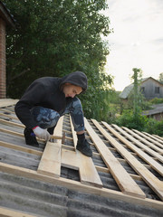 young caucasian man repairing the roof of a home; A worker replaces metal slate on the roof of a home