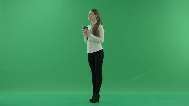business woman is drinking a cup of coffee or tea. She wears formal dress: white shirt and blak trousers. Businesswoman think, got idea and smile over green screen