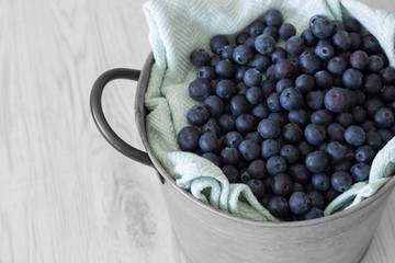 Blueberries with a tea towel in a metal pot container with handle.  Grey wood background.
