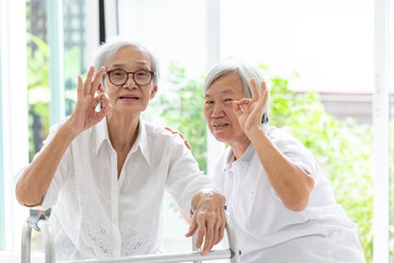 Happy two asian senior women showing ok sign with hand and fingers together,excellent symbol,friends of elderly woman or sister smiling positive with walker,friendship of the old people,retirement age