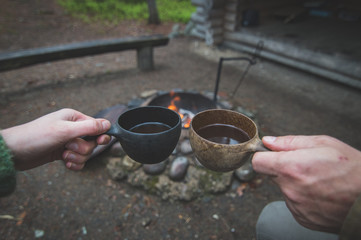 Fototapeta na wymiar Two hands holding coffee cups outdoors by the campfire