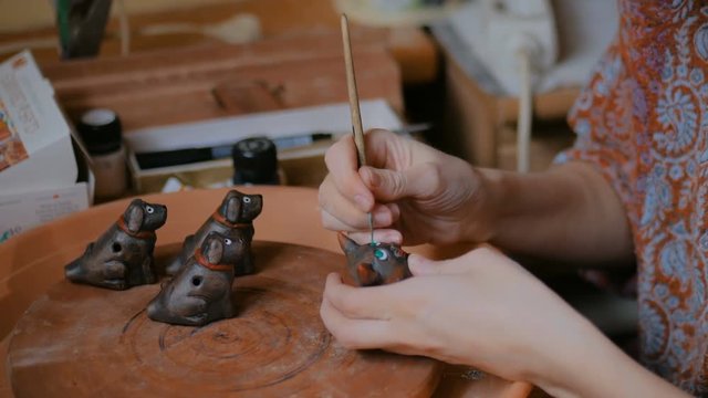 Professional woman potter, decorator painting ceramic souvenir penny whistle toy cat in pottery workshop, studio. Crafting, artwork and handmade concept