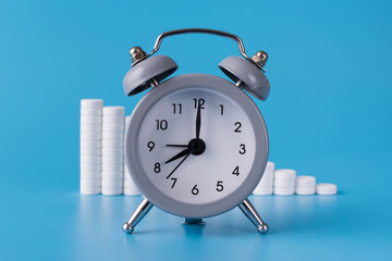 clock with alarm clock stand on a blue background and show the exact time for the taking of medicines next to them; medical talbetas are laid out for the treatment of diseases