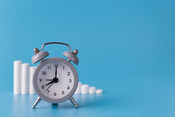 clock with alarm clock stand on a blue background and show the exact time for the taking of medicines next to them; medical talbetas are laid out for the treatment of diseases