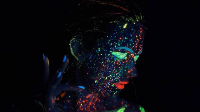 Closeup face of beautiful brunete woman in neon light. face painted with glow in the dark paint.