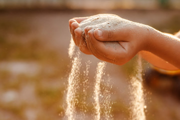 Children's hands release the falling sand. Sand flowing through your hands in the sunset sunlight.