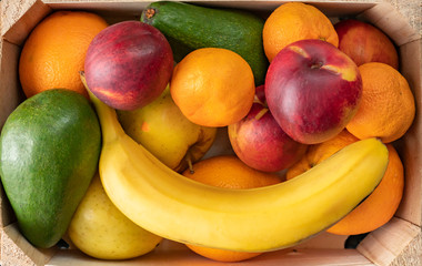 big wooden crate with ripe fresh fruits, banana, apple, orange, mandarine, avocado, vegeterian foods