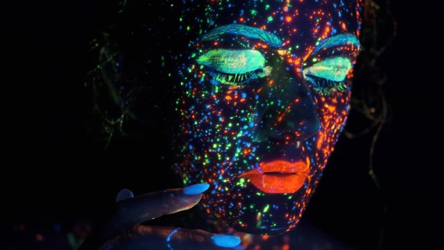 portrait of a young woman in ultraviolet light. face of the model is painted with glowing colors.