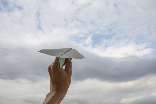 Human hand launching paper plane in cloudy sky