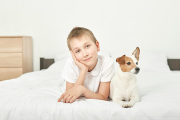 boy with dog jack russell sitting on a white bed at home
