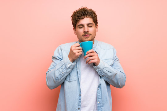 Blonde man over pink wall holding a hot cup of coffee