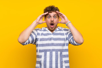 Blonde man over yellow wall with surprise and shocked facial expression