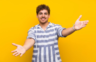 Blonde man over yellow wall presenting and inviting to come with hand