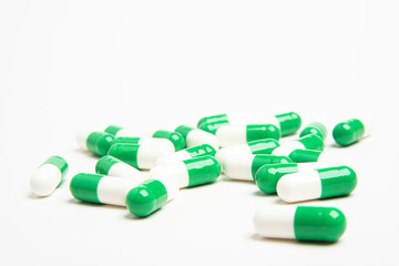 A bunch of green and white medicine capsules artistically set on a plain white background.