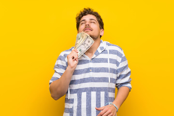 Blonde man over yellow wall taking a lot of money