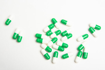 A bunch of green and white medicine capsules artistically set on a plain white background.