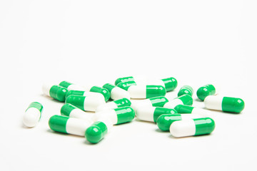 A bunch of green and white medicine capsules artistically set on a plain white background.