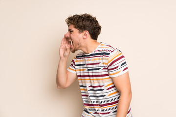 Blonde man over isolated wall shouting with mouth wide open to the lateral