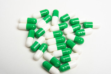 A bunch of green and white medicine capsules artistically set on a plain white background.