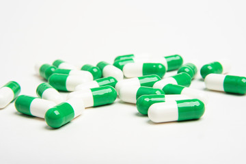 A bunch of green and white medicine capsules artistically set on a plain white background.