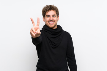 Fototapeta premium Blonde man over isolated white wall smiling and showing victory sign
