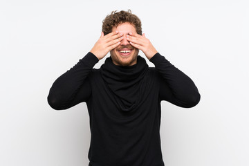 Blonde man over isolated white wall covering eyes by hands