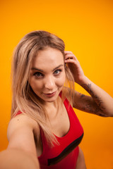 Fototapeta premium Beautiful young woman with fit body in swimming suit taking a selfie and playing with her hair over yellow background