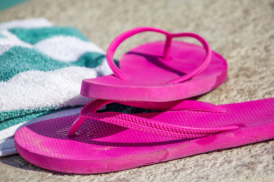 Pink slippers and towel on a pool deck
