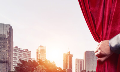 Modern business cityscape behind curtain opened by businessman hand